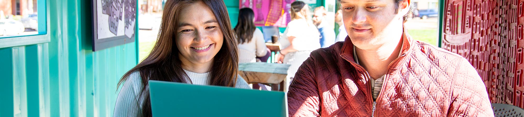 A young woman and man looking at the screen of a laptop computer in a cafe environment