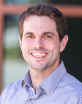 Headshot of Adam Crary wearing a button-down business shirt and smiling in an outdoor setting.