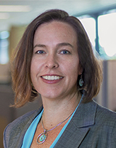 Amy Sirmans smiles while wearing a blue shirt and grey jacket.