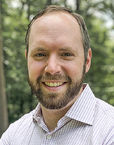 Andrew White in a pinstripe shirt standing in the woods 