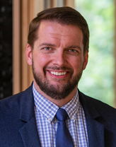 Benjamin Martin smiling in a checkered shirt and navy blue blazer.