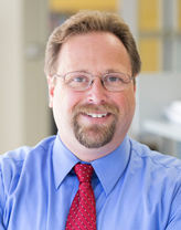 Chris Bobay smiling in a baby blue shirt and red tie.