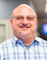 Frank Koczalk smiling in a blue and white checkered shirt.