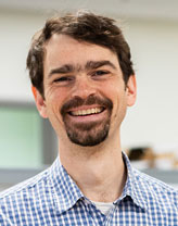 Headshot of Jacob Flanigan wearing a button-down business shirt and smiling in an office setting.