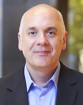 Joe wearing a navy blazer and blue shirt in front of a blurred background.