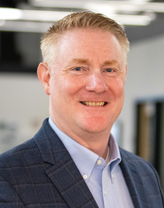 John Hapkiewicz smiling in a dark gray stripped blazer.