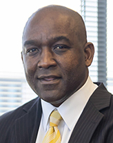 Reggie Scales sits at his desk in a black sports coat and yellow tie.