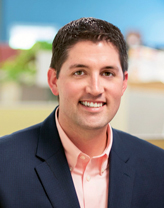 Richard Wiatt smiling in a navy blue jacket and pink shirt.