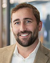 Seth at the office, wearing a white shirt and tan blazer.