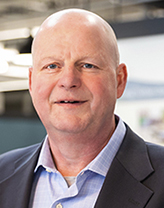 Tim Patch smiling in dark suit and striped shirt