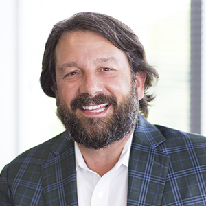 Kris Dramby, wearing a white shirt and plaid blazer, smiles in the office.