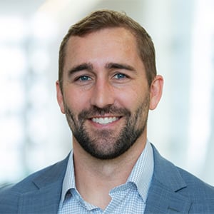 Seth at the office, wearing a white shirt and tan blazer.