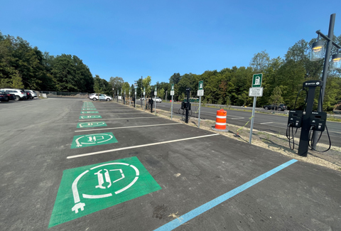 Rows of green-signage marking EV charging stations in a parking lot under a blue sky. 