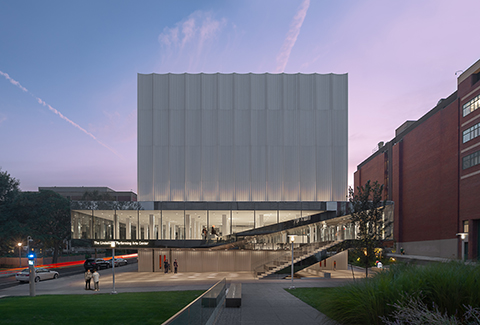 A digital rendering of Brown University’s new Performing Arts Center surrounding a green space with trees and students walking across a crosswalk.