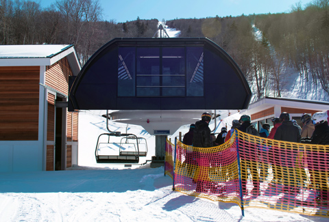 View of the high speed lift in the wintertime with skiers lined up in the queue to get on the list. 