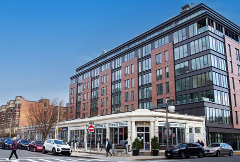 A multistory glass and brick building atop retail space near a playground.