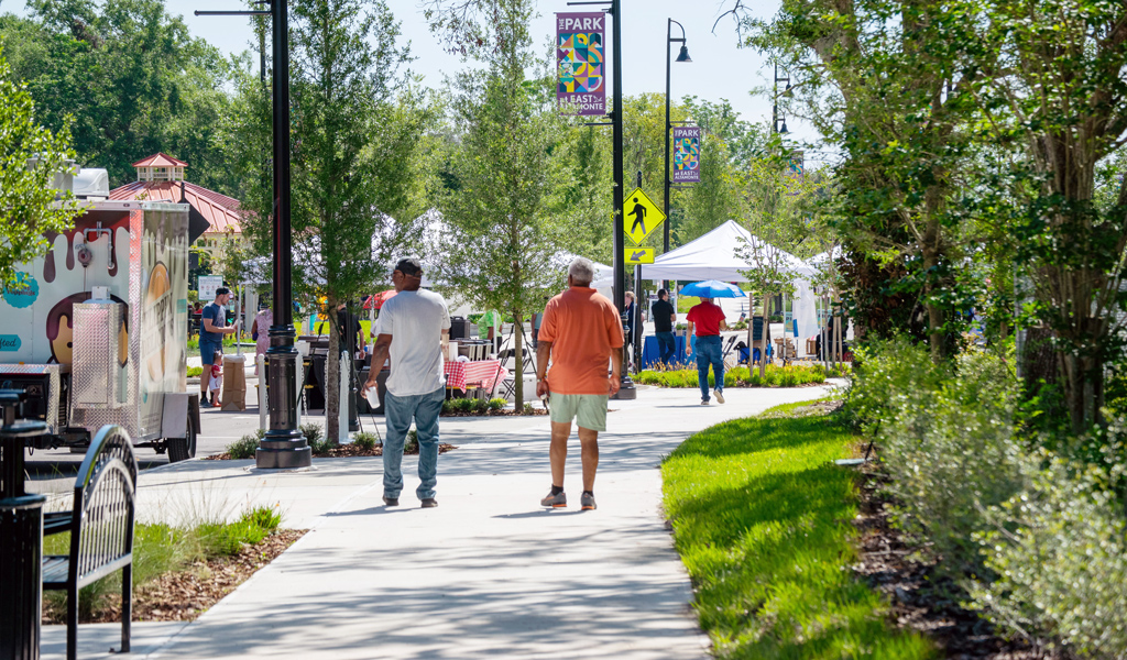 People walk on a park sidewalk past tents and food trucks.