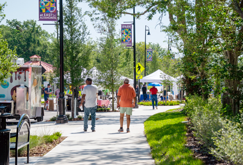 People walk on a park sidewalk past tents and food trucks.