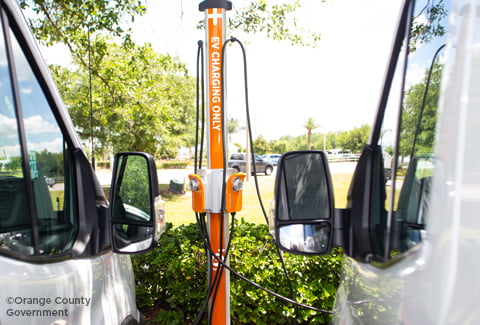 Two white vans plugged in to an outdoors electric vehicle charging station