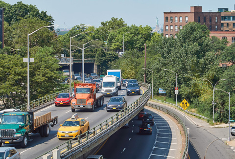 Cars and trucks driving on a highway in New York City with Statue of Liberty in the distance.