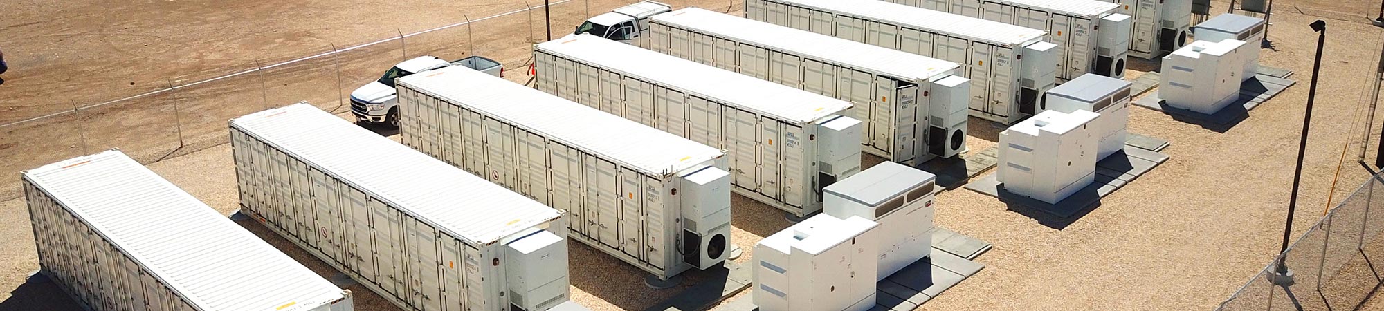 A row of eight (8) battery energy storage system units surrounded by a fence.