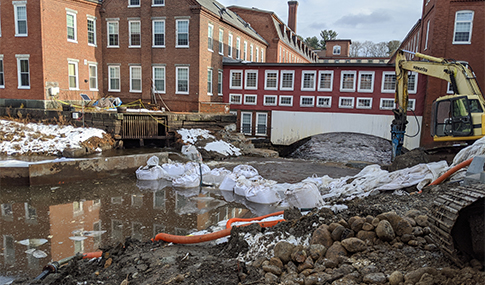 An excavator removes the granite masonry blocks of the dam that had blocked a river.