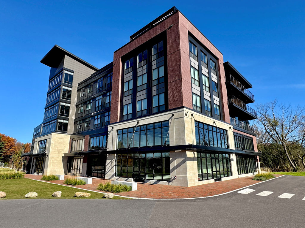 Corner view of a large modern commercial building fronted by a parking lot and a lawn.