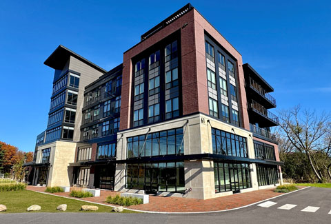 Corner view of a large modern commercial building fronted by a parking lot and a lawn.