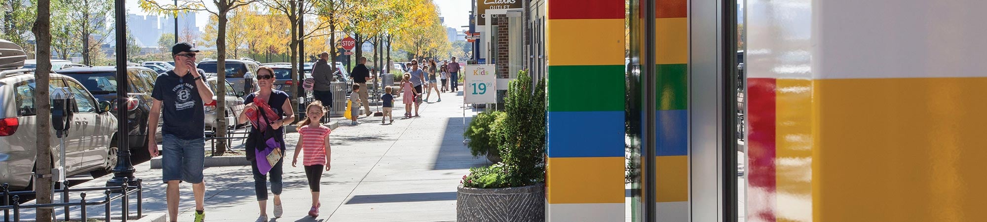 Families walk along a bustling sidewalk in a mixed-use development.