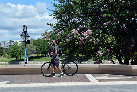 A person walking his bike on a sidewalk.