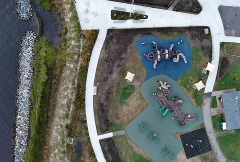 Aeriel view of playground at Shorefront Park, surrounded by green space and walking paths near the shoreline.