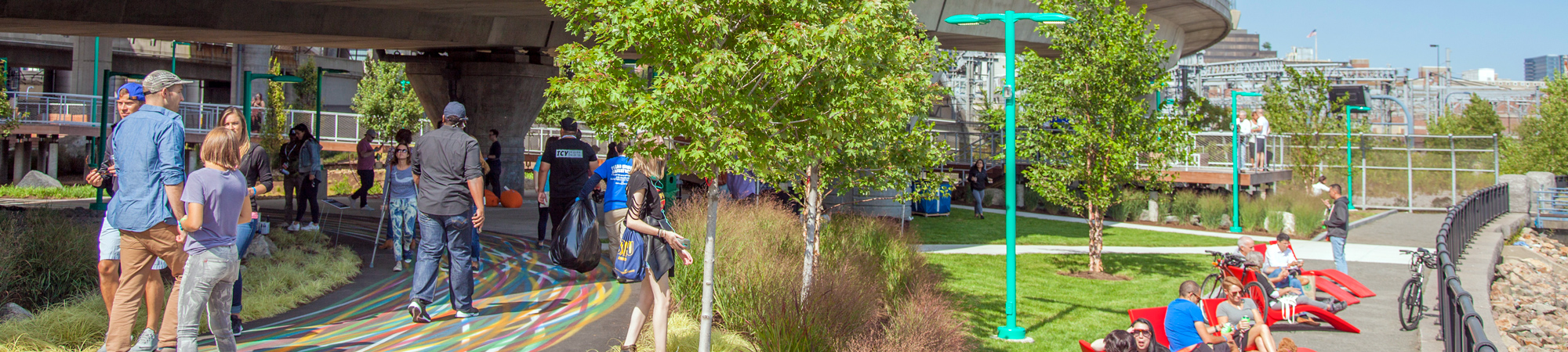 People walking and enjoying outdoor recreation in green space beneath an interchange.