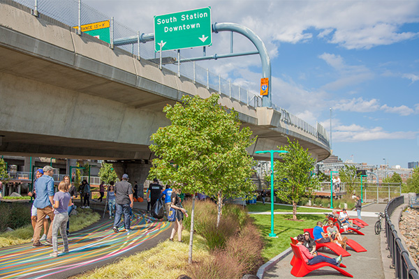 People walking and enjoying outdoor recreation in green space beneath an interchange.