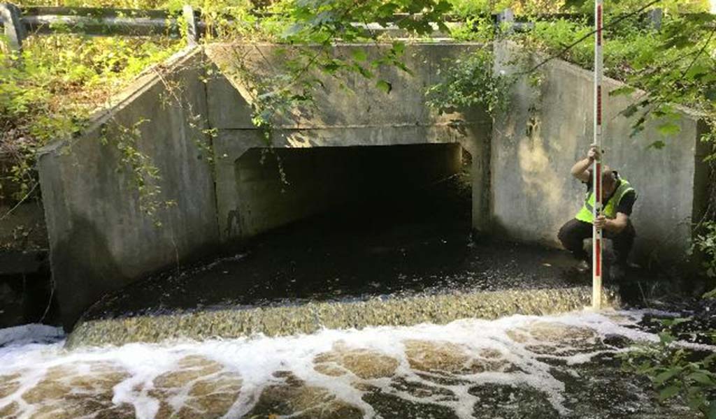 A man measuring water level of a stream under a road.