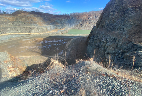 Landscape view down into the quarry with hills filled with gray gravel and a blue-green pond at the bottom. 