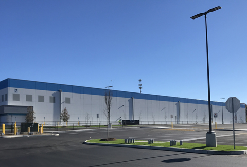 Exterior view of a large warehouse with a spacious parking lot under a clear blue sky.