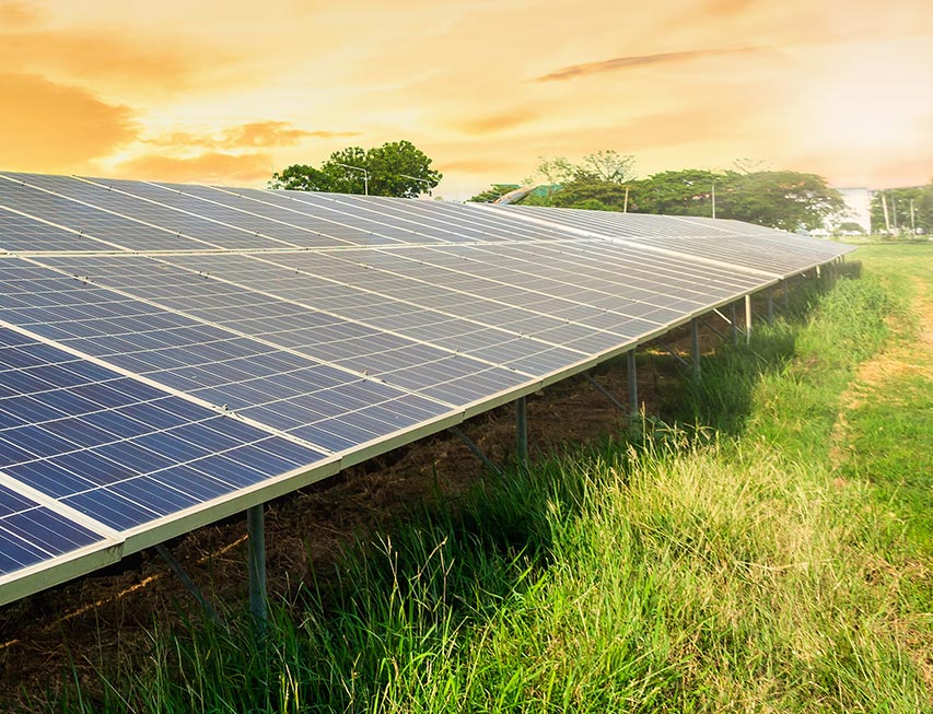 A solar panel in a field with the sun setting in the background. 