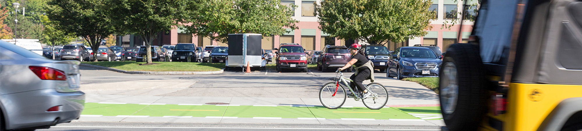 Woman rides bicycle on green bike lane separated from cars.