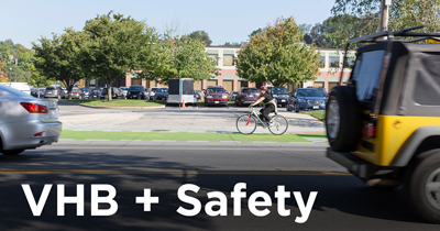 Woman rides bicycle on green bike lane separated from cars.