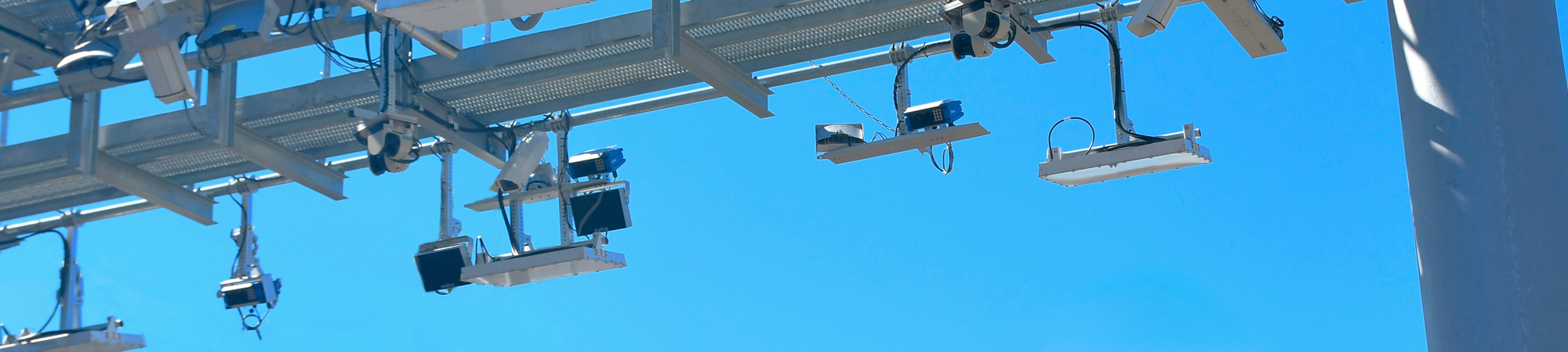 A woman in a hardhat and safety vest looks up towards a toll gantry.