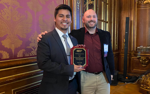 Alvaro Calle smiles at the camera holding his award plaque.