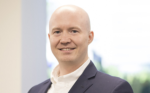 Andrew Buck smiling in a white shirt and blue blazer.