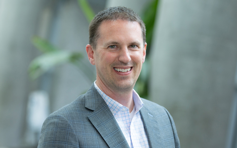 Andrew Burkholder smiling in a gray blazer and checked collared shirt.