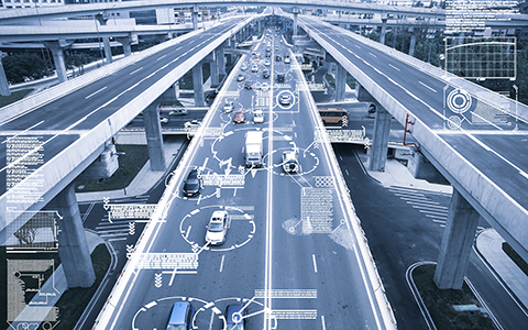 Cars drive along a five-lane highway. Computerized circles and lines appear around the cars to display a traffic management system. 