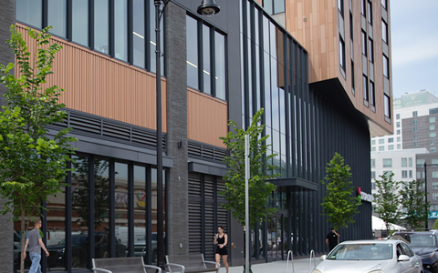 A close-up on a multi-story building with a Stop and Shop sign on the bottom level, with pedestrians on the adjacent sidewalk.