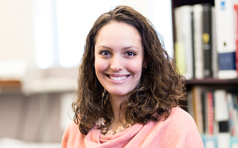 A photo of Brittany Gesner, a woman with curly brown shoulder length hair in a pink shirt. 