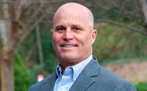 Chris Crow is standing outside wearing a blue shirt and jacket.