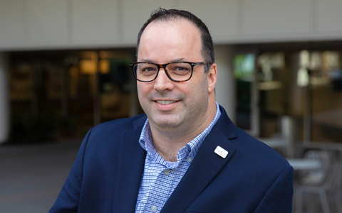 Dave Mulholland wearing glasses, a blue collared shirt and a jacket