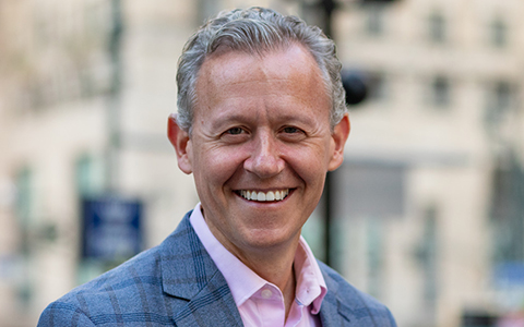 David Quart smiling in a blue suite and pink shirt.