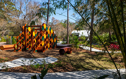 Nature path through bamboo with orange hexagon bench in foreground.